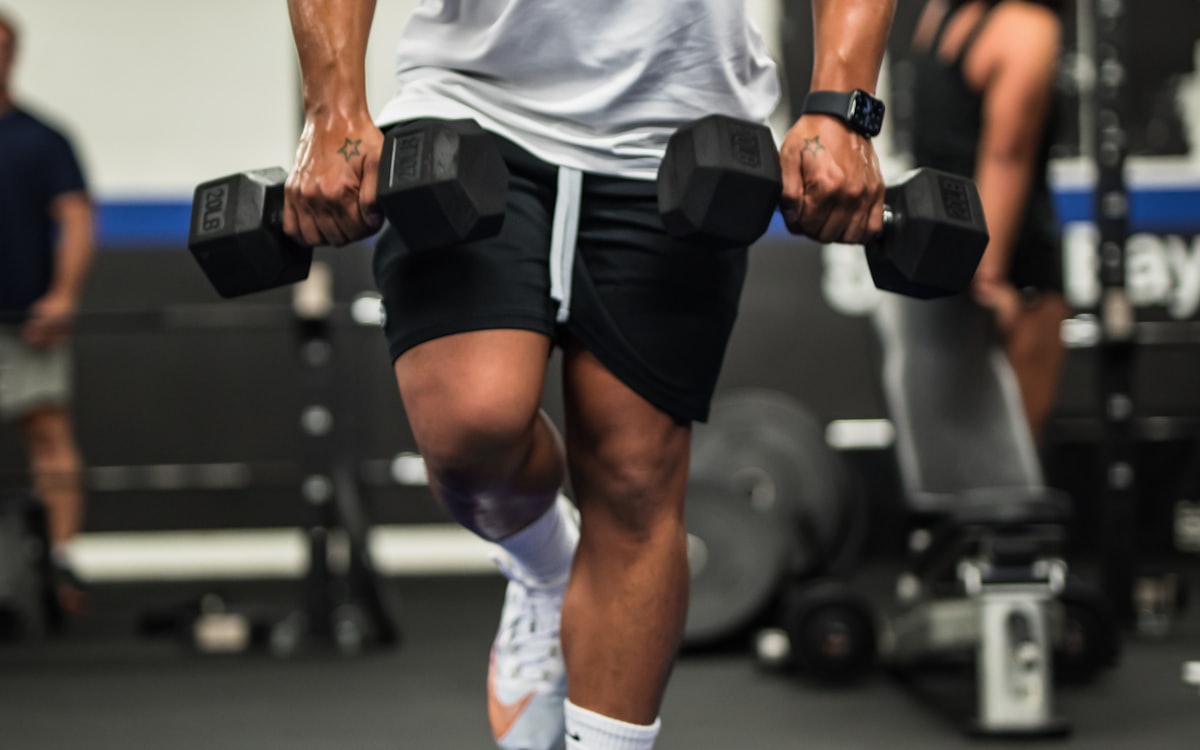 A man carrying dumbbells through a lunge, seen from the shoulders down